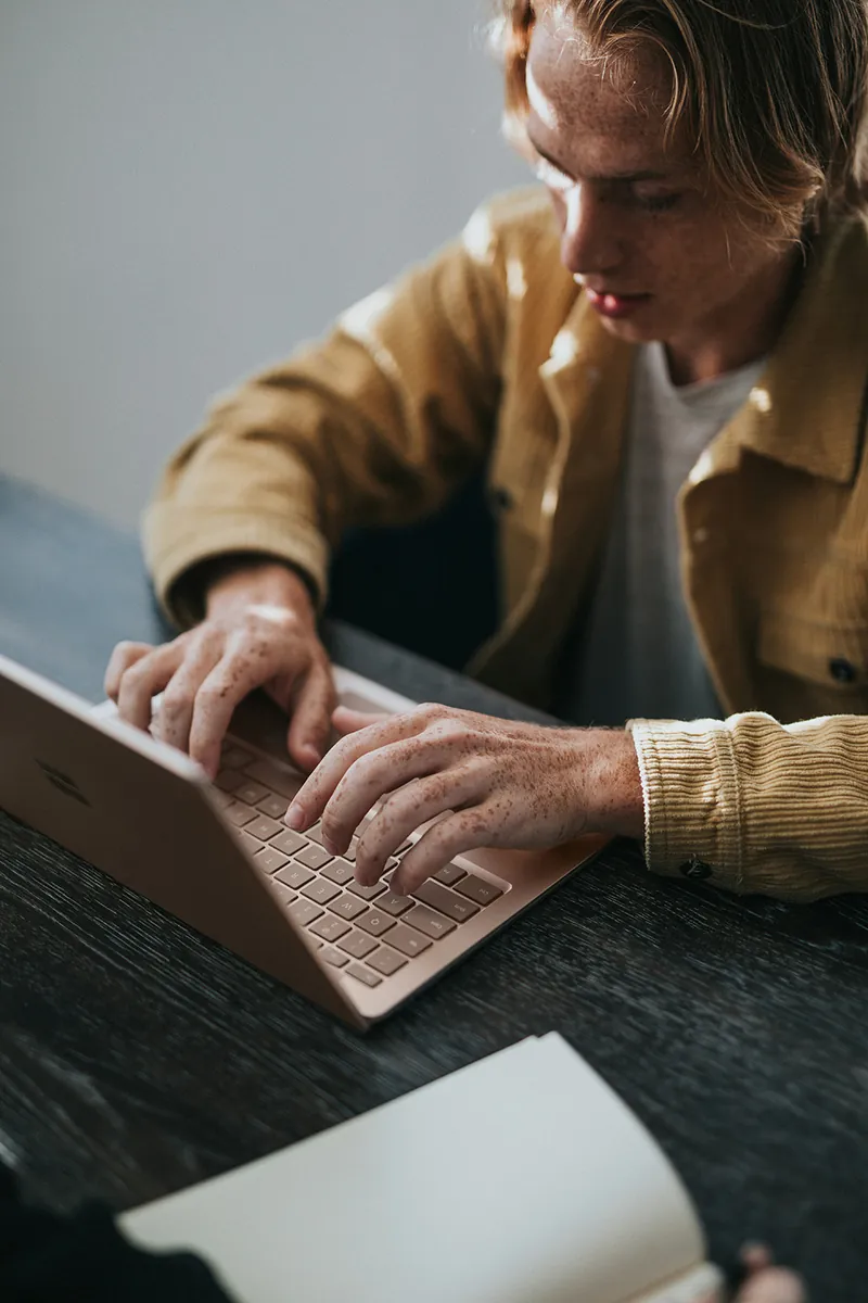 A developer typing on a laptop at a wooden desk